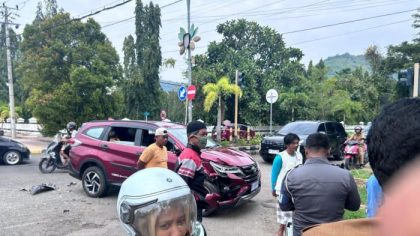 Mobil Toyota Rush merah marun mengalami kerusakan parah di bagian depan setelah tabrakan di simpang empat Belopa, dikelilingi warga yang menyaksikan kecelakaan.