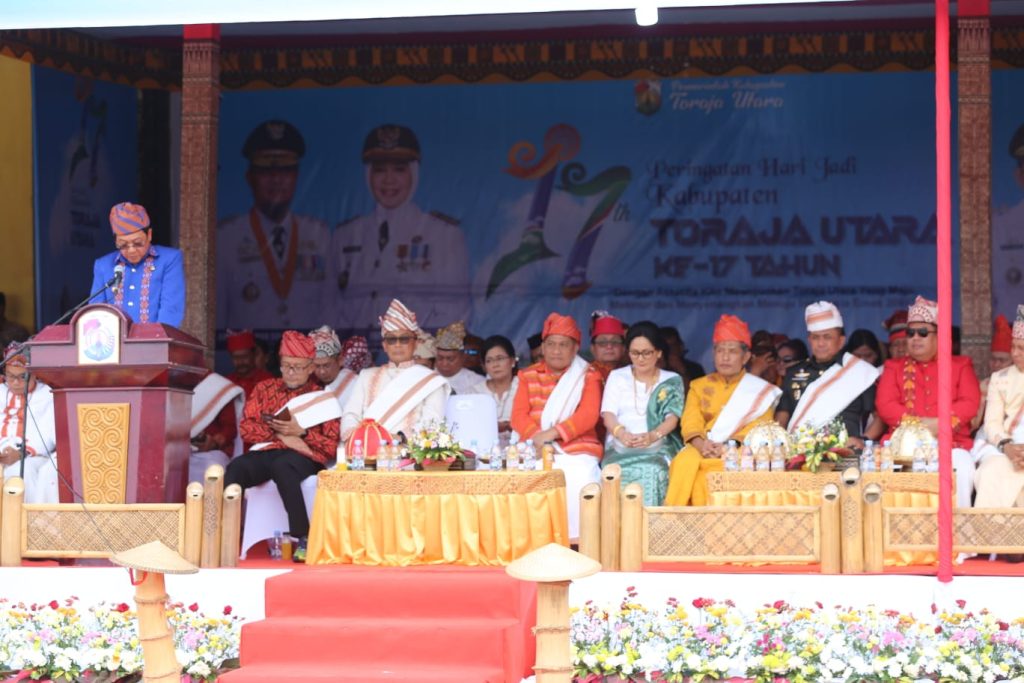 Bupati Toraja Utara Frederik Viktor Palimbong menyampaikan sambutan di atas panggung perayaan HUT ke-17 Toraja Utara, didampingi para tokoh masyarakat dan pejabat yang mengenakan pakaian adat Toraja.