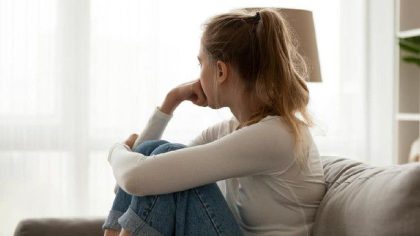 Seorang perempuan muda duduk termenung di sofa, menggambarkan suasana hati yang tidak stabil akibat gangguan bipolar.