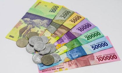Tumpukan uang rupiah pecahan lima puluh ribu dan seratus ribu dipegang tangan sebagai simbol redenominasi rupiah